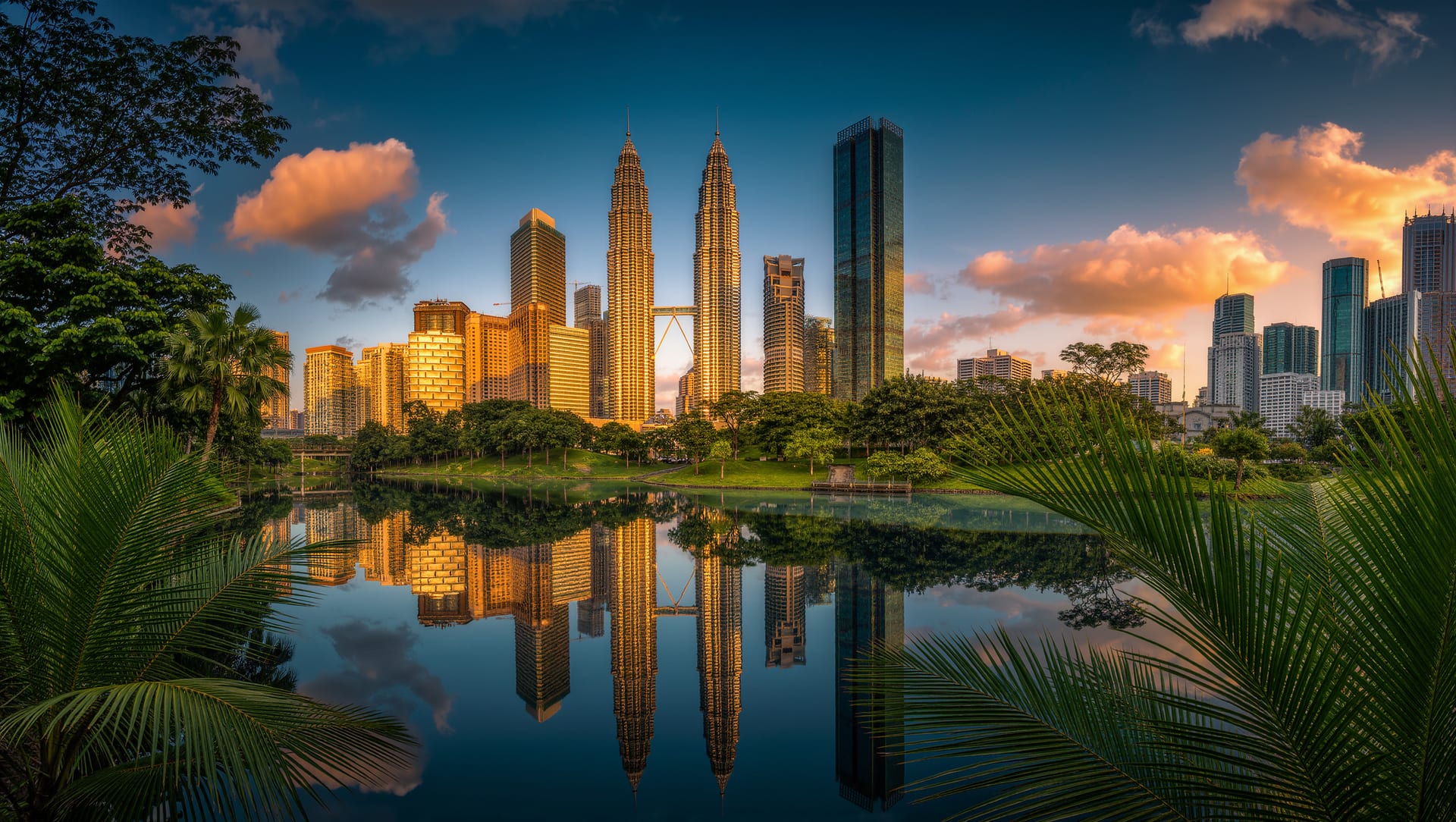 The Kuala Lumpur skyline with the Petronas Towers at dusk, reflected in a lake fringed with palms
