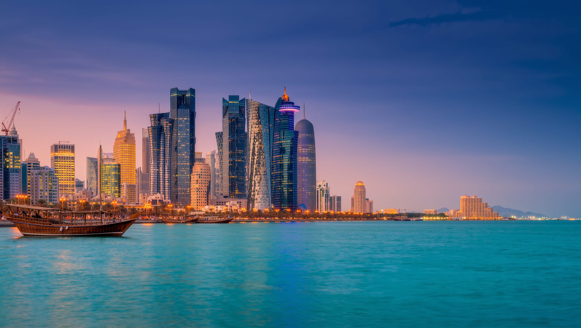 The Doha West Bay skyline at dusk seen across the bay, with a dhow on the water