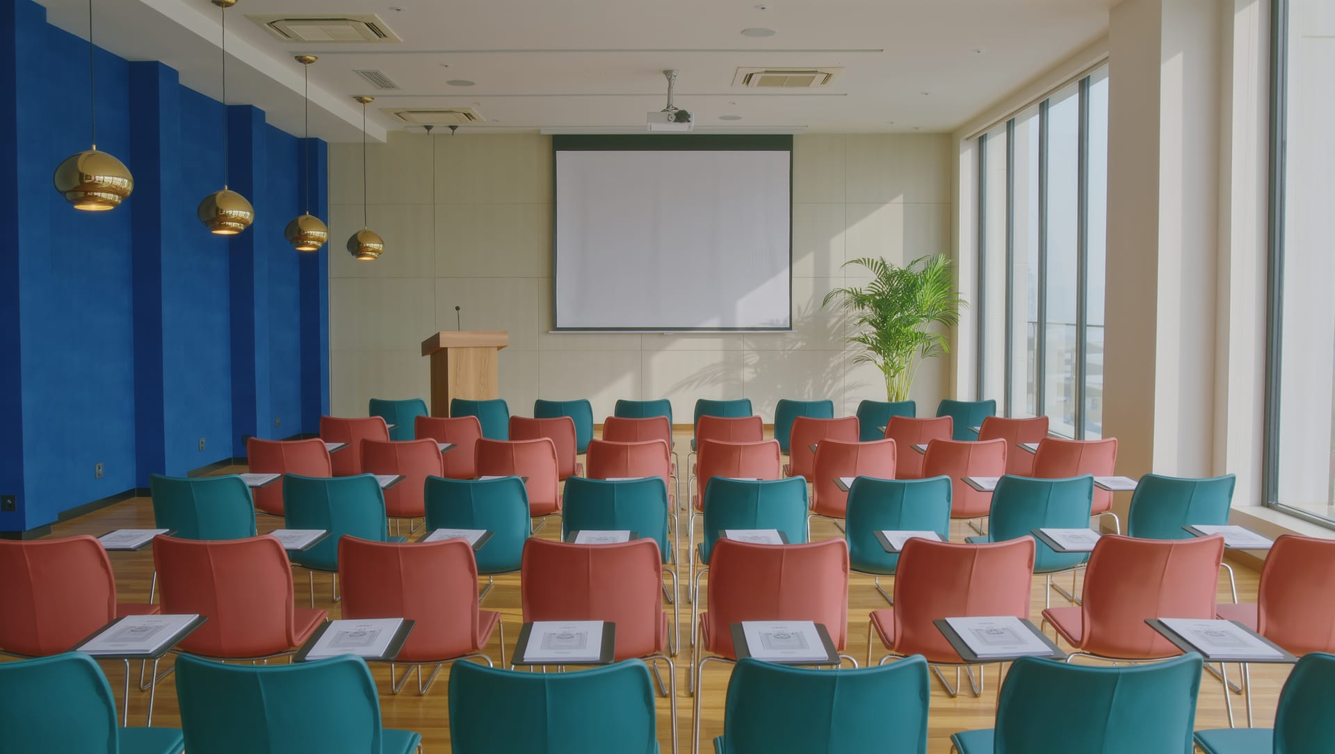 An empty training room set out for a pre-departure briefing — rows of teal and coral chairs facing a projector screen