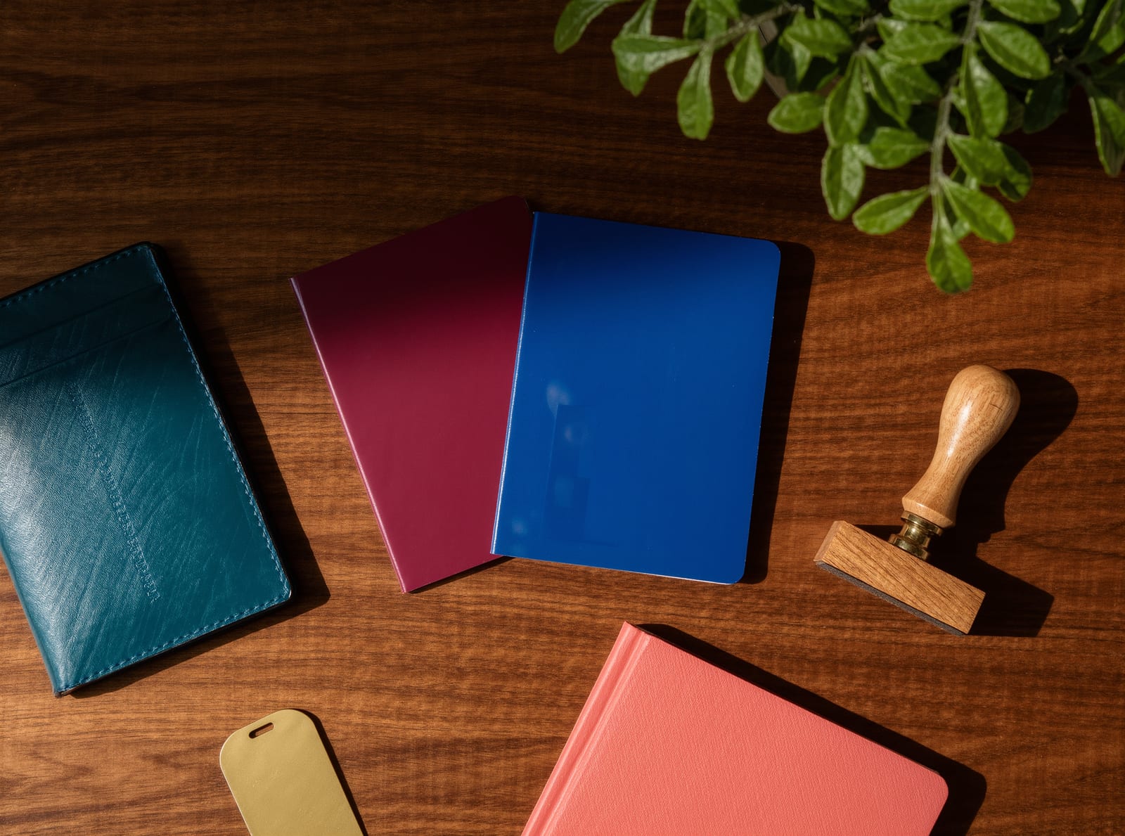 Teal, crimson, blue and coral passport wallets laid out on a dark timber desk beside a wooden stamp